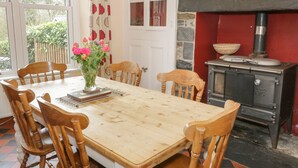 A dining room with a wooden table, chairs, a vase with flowers, a window, and a wood-burning stove. - Ty Capel (Betws-Y-Coed)