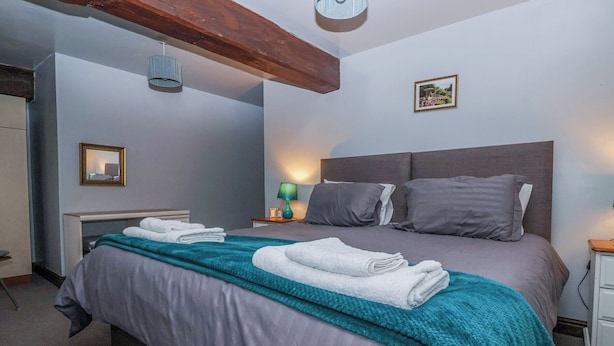 A neatly made bed with a teal blanket and white towels, a bedside lamp, and a framed picture on the wall. - Rose (Selby)