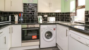 A modern kitchen with white cabinets, a microwave, an oven, a washing machine, and a sink. - Rose (Selby)