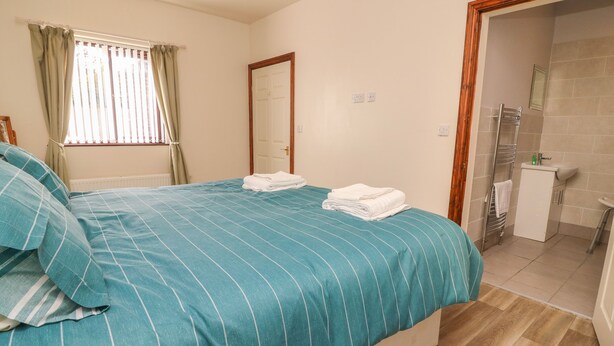 Un dormitorio con cama, un baño con lavamanos y espejo, y una puerta que da a otra habitación.