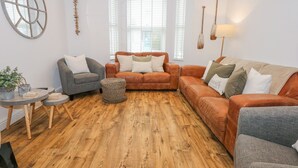 A cozy living room with a wooden floor, two sofas, a grey armchair, and a small round table with a plant.