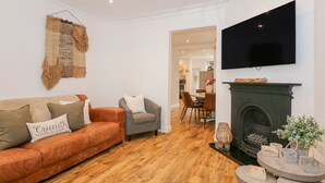 A living room with a sofa, armchairs, a fireplace, and a TV mounted on the wall.