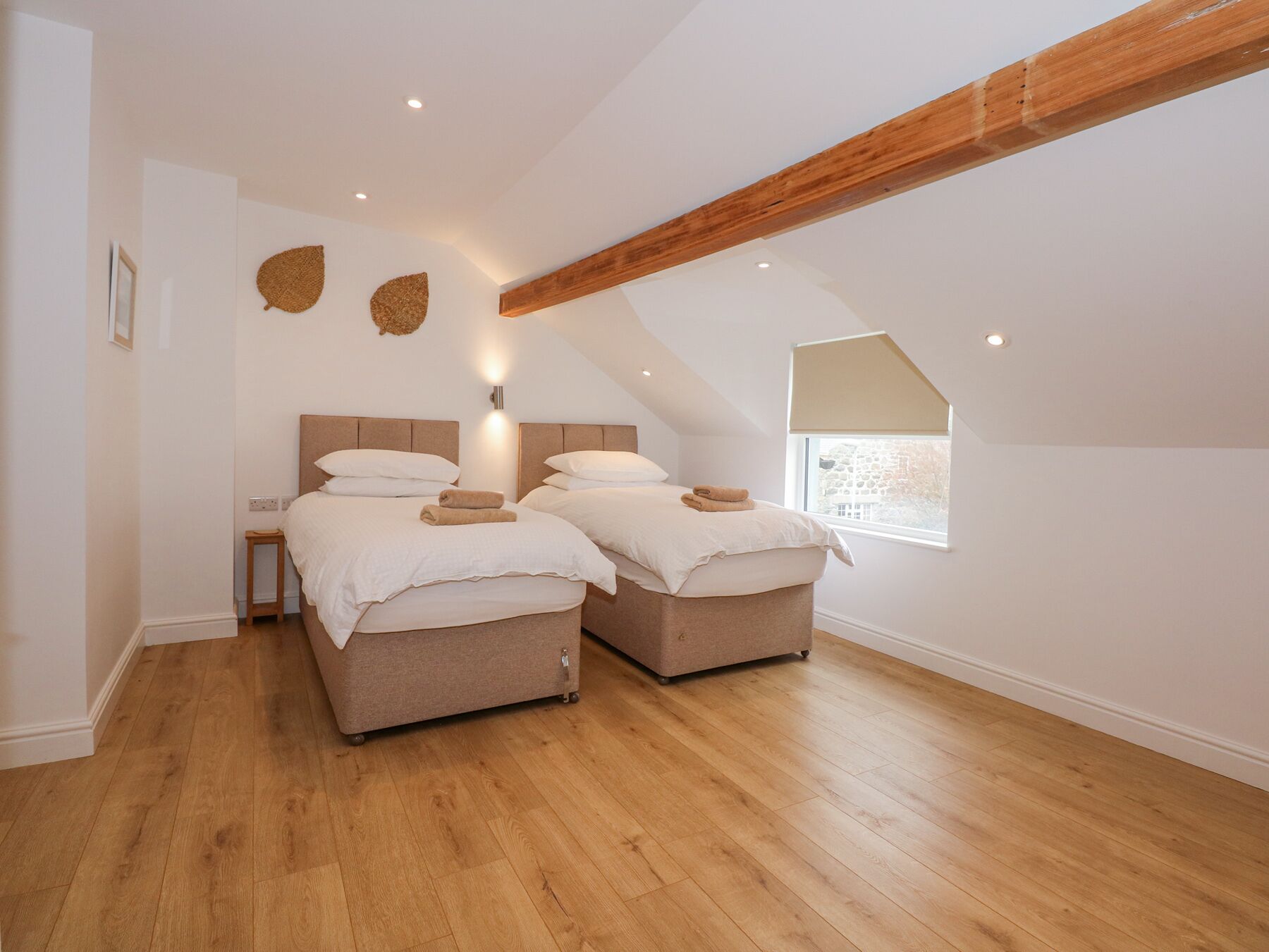 Un dormitorio con dos camas, vigas de madera, un ventanal pequeño y una lámpara fijada a la pared.
