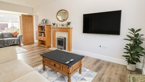 A living room with a fireplace, a TV mounted on the wall, a sofa, a coffee table, and a bookshelf. - The Croft Bungalow (Wigton)