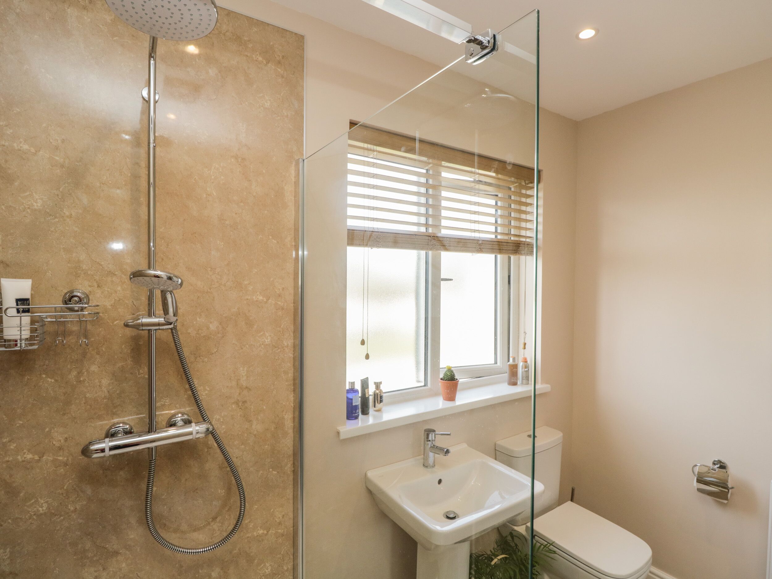 A modern bathroom with a glass-enclosed shower, a sink, a toilet, and a window with blinds.