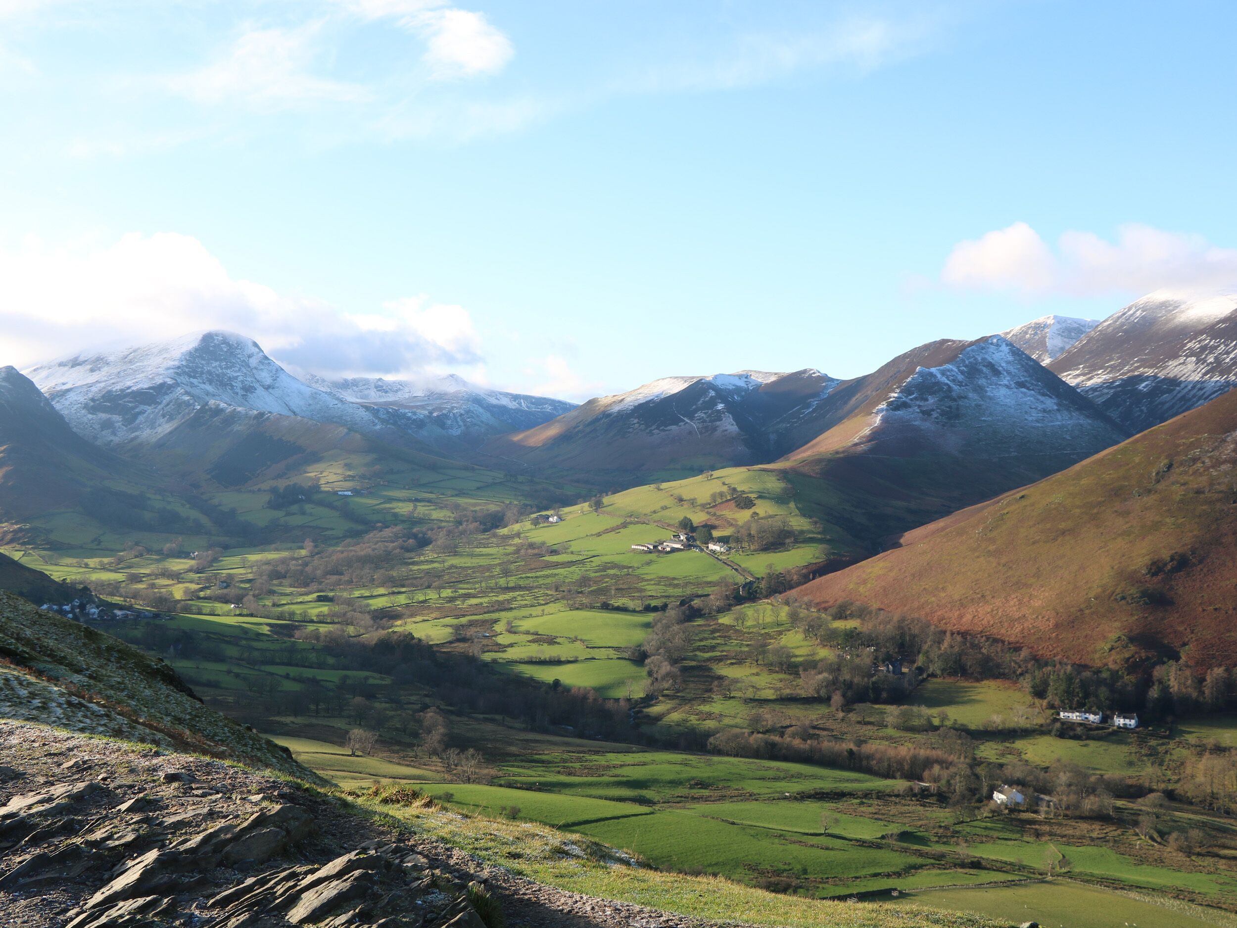 A valley with green fields, a small house, and snow-capped mountains in the background.