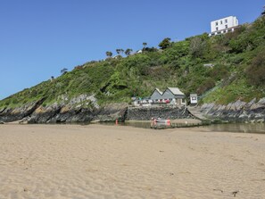 A beach with a building on a hill, a small dock, and a sandy shore. - Eloen (Newquay)