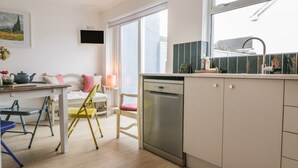 A modern kitchen with a dishwasher, a dining area with a table and chairs, and a large window providing natural light. - Eloen (Newquay)