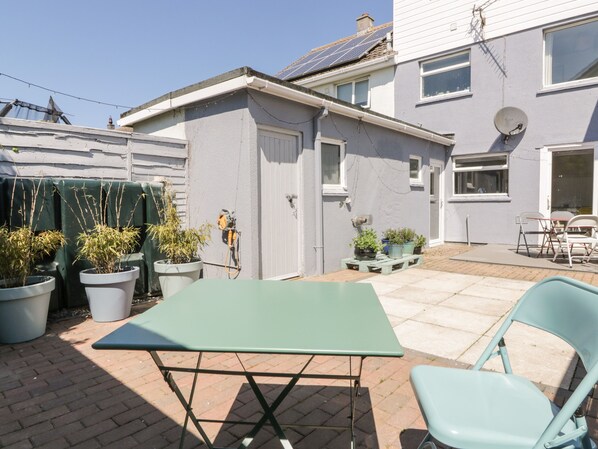 A patio area with a green table and chairs, potted plants, and a solar panel on the roof. - Eloen (Newquay)