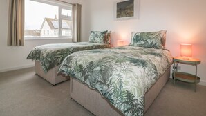 A bedroom with two beds, a window, a lamp, and a painting on the wall. - Eloen (Newquay)