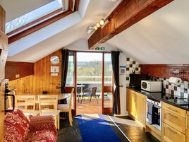 Una habitación acogedora con techo de madera, una mesa de comedor con sillas, un sofá, una cocina con microondas y estufa, y vistas al exterior a través de un ventanal.