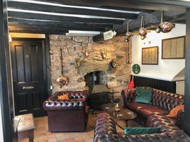 Interior acogedor de un pub con pared de piedra, sofás de cuero y un cartel que indica que es un mercado de pulgas.