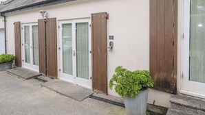 Een rij witte deuren met bruine luiken, een bloempot en een metalen huisnummer op de muur.