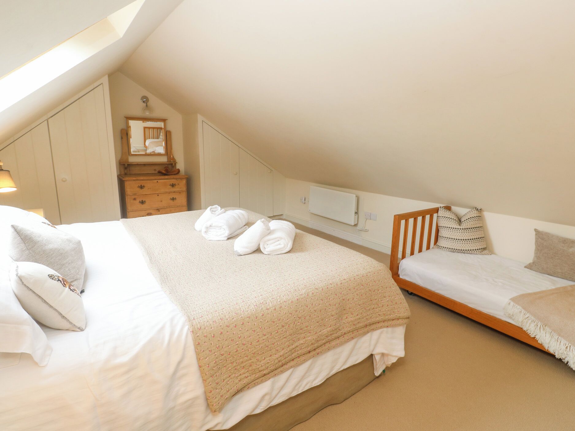 A cozy attic bedroom with a large bed, a smaller bed, and a dresser.