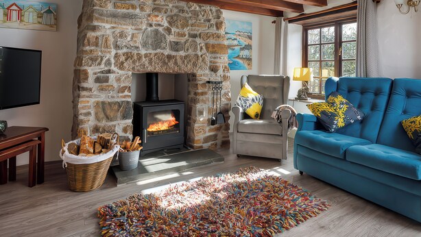 Ein gemütliches Wohnzimmer mit Kamin aus Stein, einem blauen Sofa und einem Fernseher.