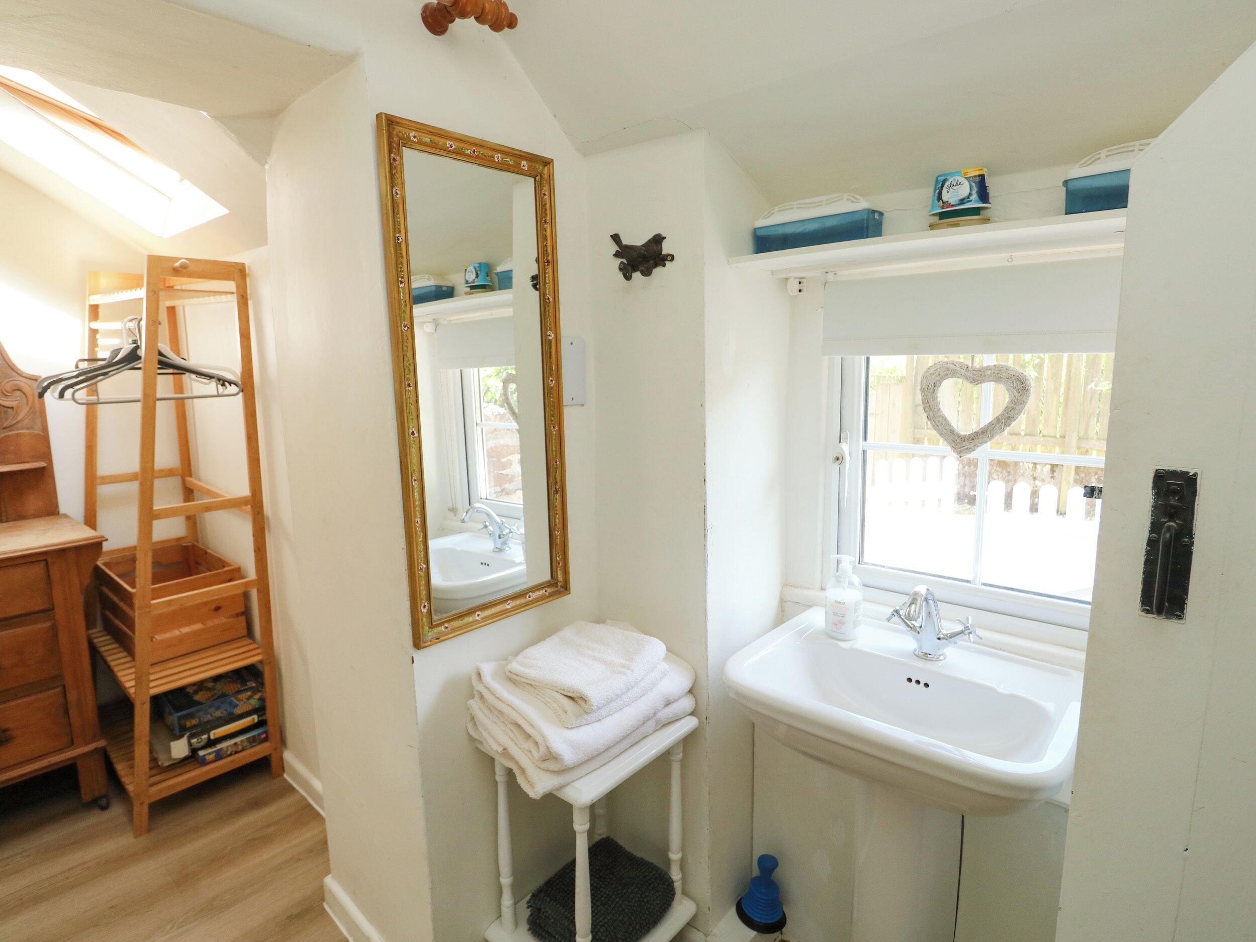 A bathroom with a wooden shelf, a mirror with a decorative frame, a sink, and a window with a heart-shaped decoration.