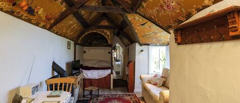 A cozy room with a wooden ceiling, a bed, a table with chairs, and a red patterned rug.