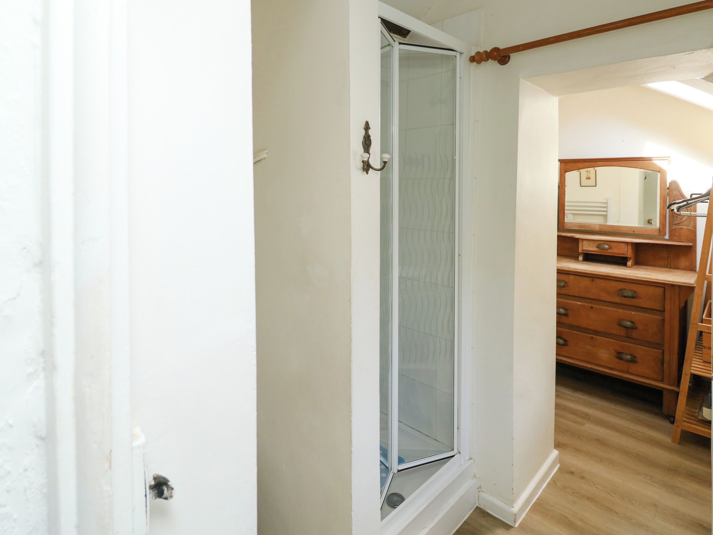 Une salle de bain avec une porte de douche en verre, une commode en bois et un miroir.