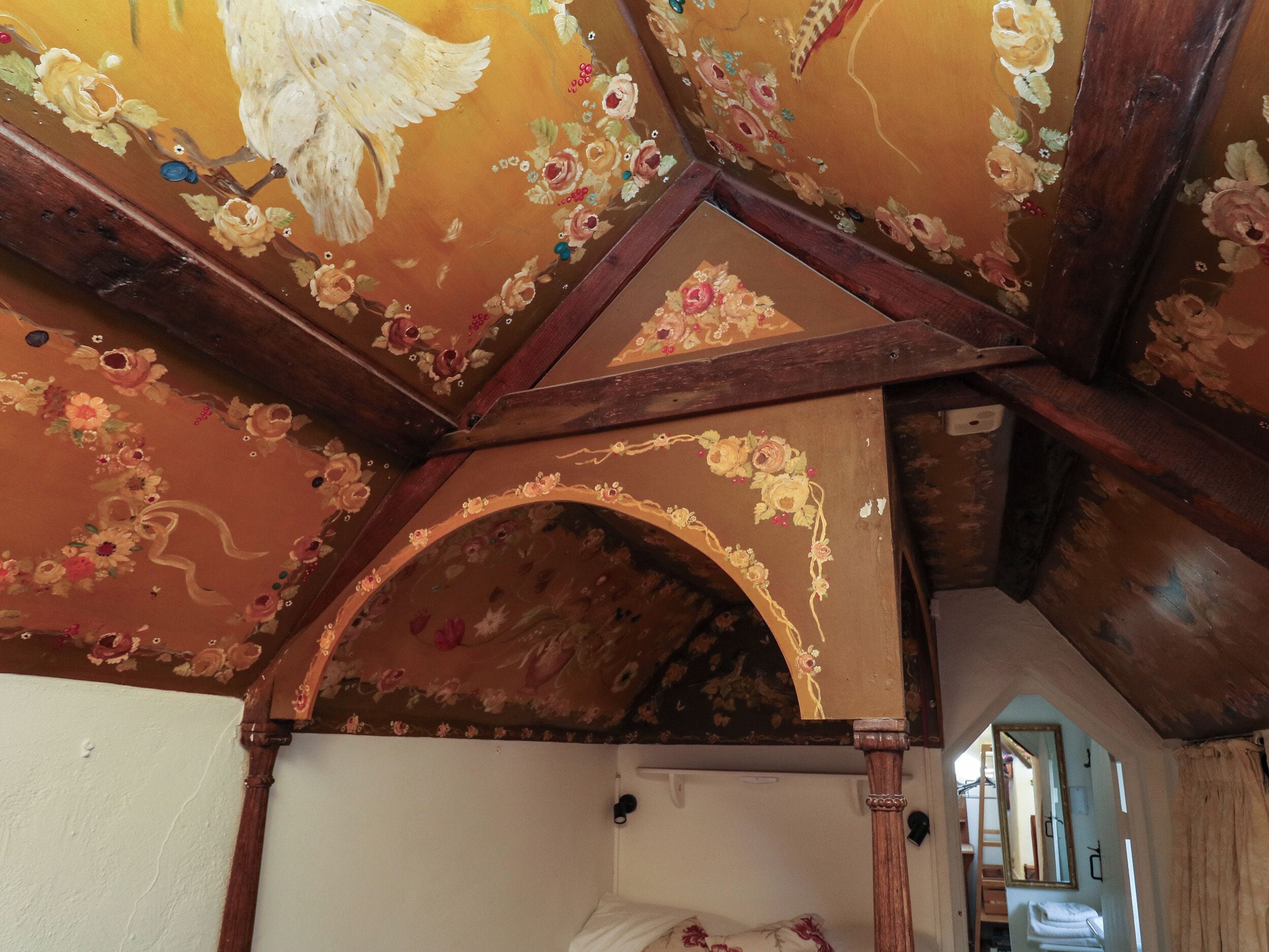Een kamer met een houten plafond met bloem- en geometrische patronen, een zichtbare boog en een bed met een bloemenbedekking.
