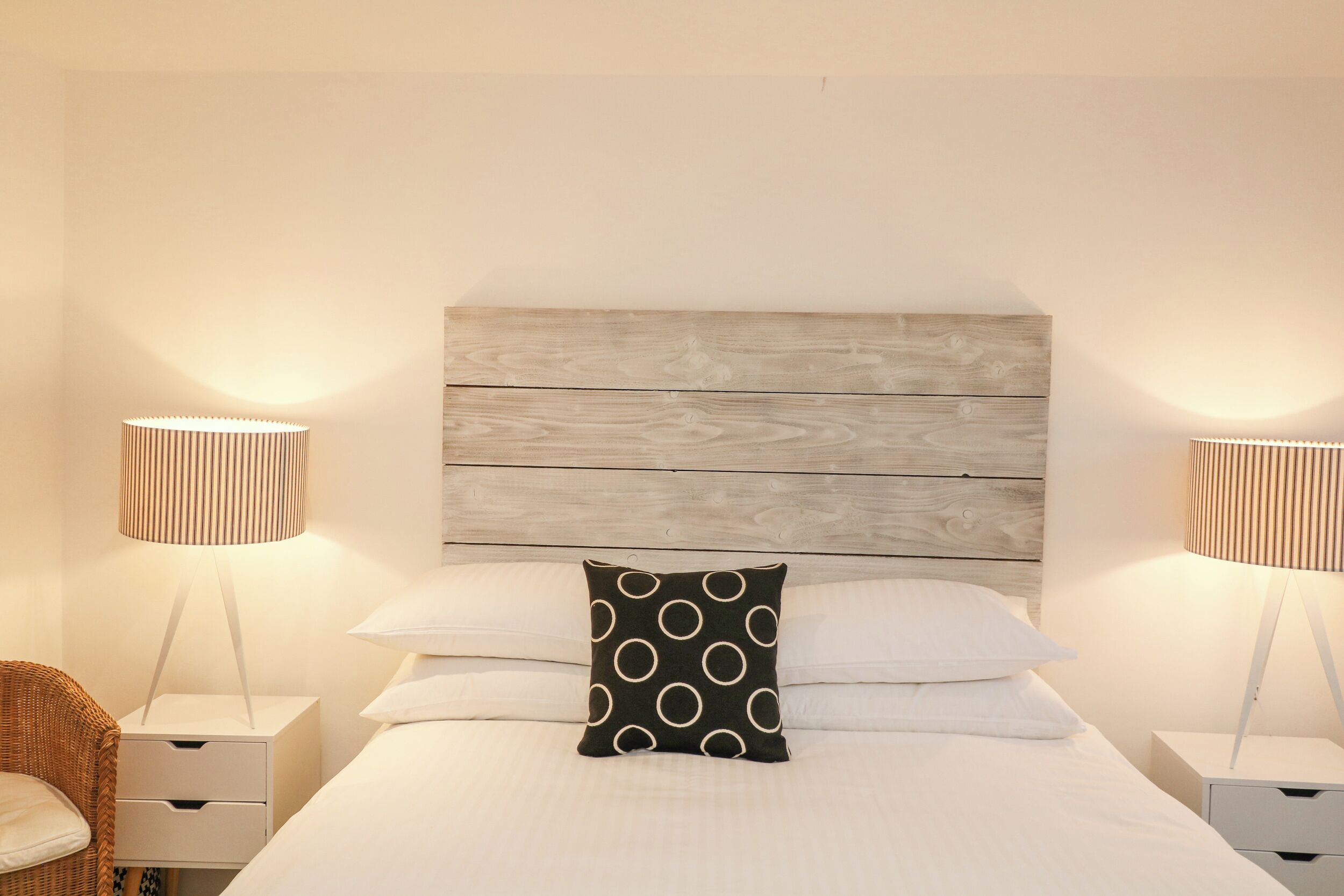 A neatly made bed with a wooden headboard, two bedside tables with lamps, and a wicker chair.