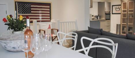 Un salon moderne avec une table blanche dressée pour le repas, un canapé gris et un grand drapeau américain accroché au mur.