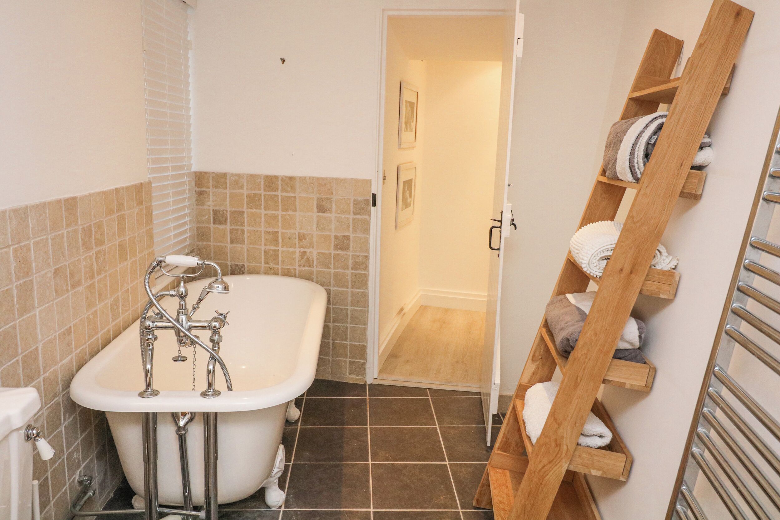 A bathroom with a freestanding bathtub, a wooden towel rack, and a tiled floor.