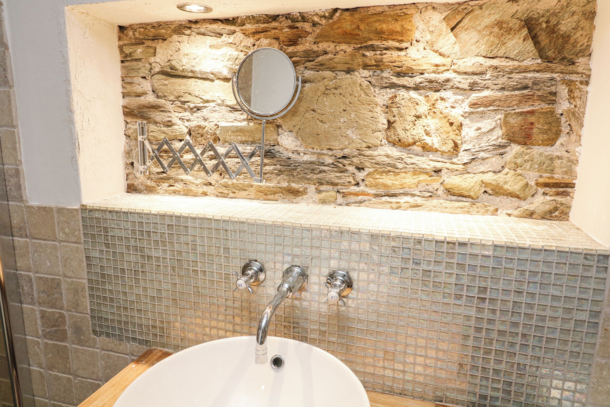 A bathroom with a stone wall, a mirror, and a tiled sink.