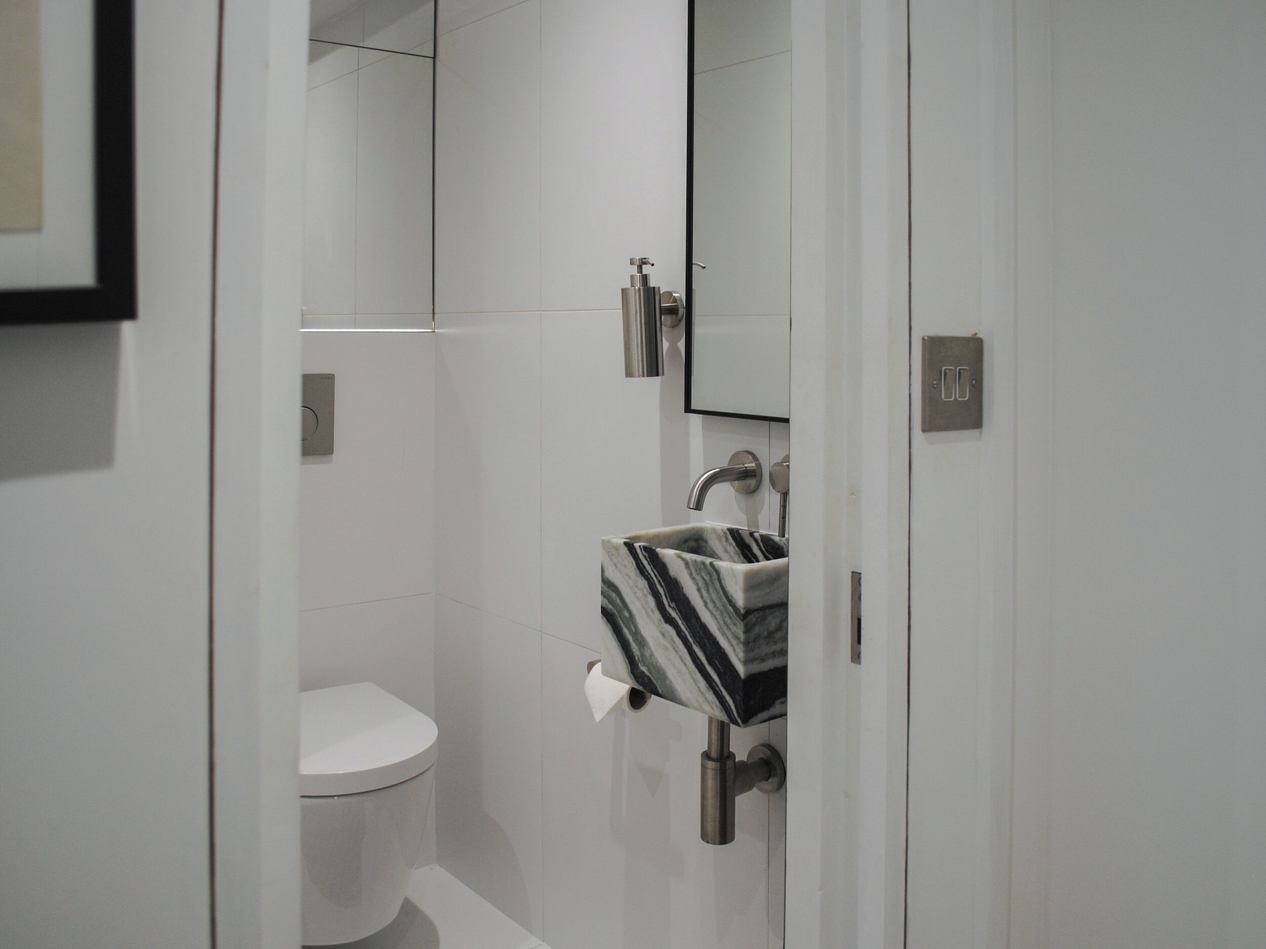 Une salle de bain moderne avec des toilettes blanches, un lavabo en marbre et un miroir.