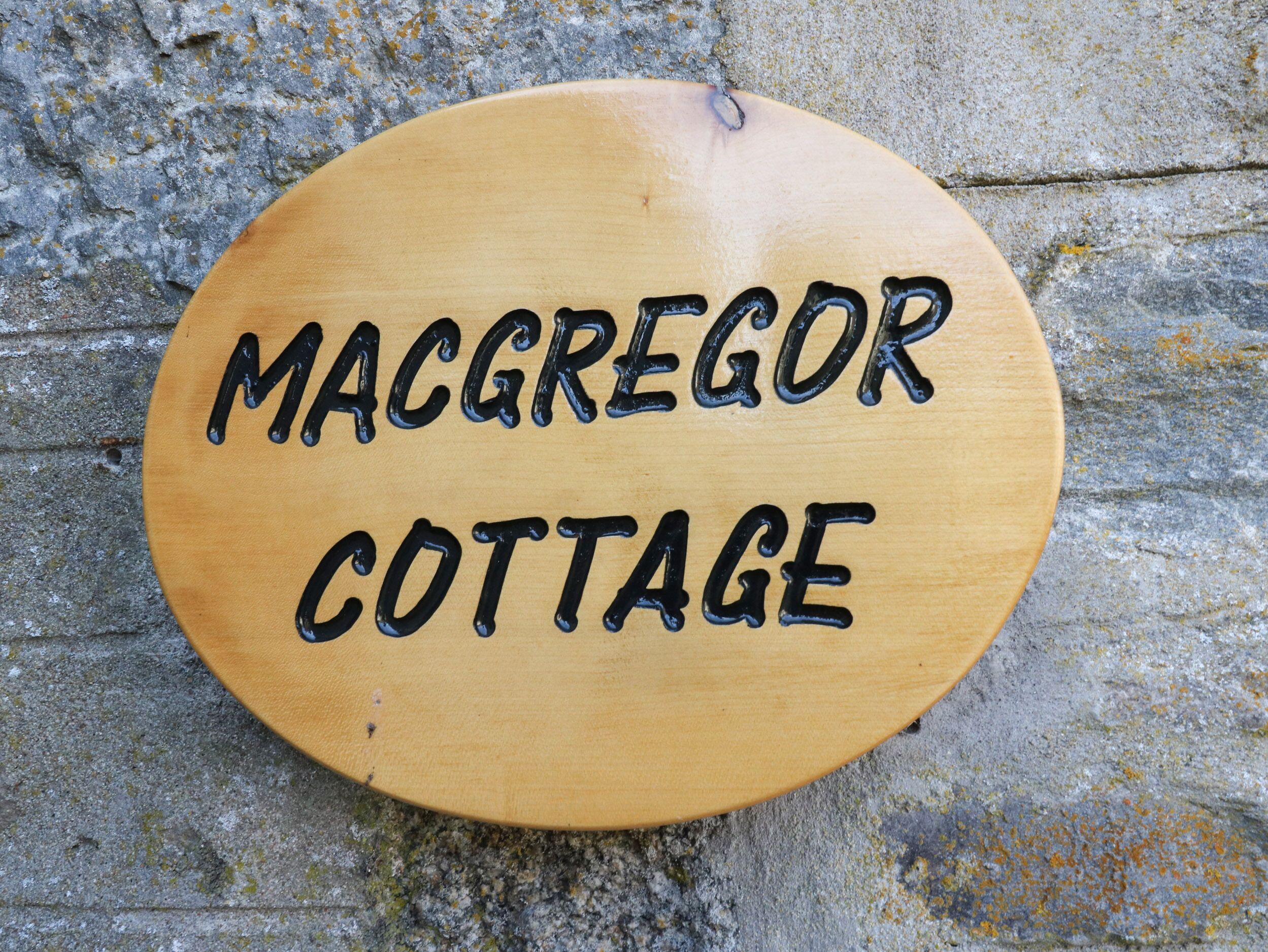 Une enseigne en bois portant l’inscription « MACGREGOR COTTAGE » sur un fond de pierres.