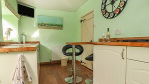 A kitchen with a wooden countertop, a sink, a radiator, a stool, and a clock on the wall. - Cobblers Cottage (Keighley)