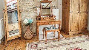 A rustic room with a wooden dresser, a mirror, a small table, and a wicker vase with flowers. - Cobblers Cottage (Keighley)