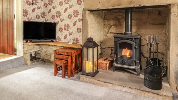 A cozy room with a stone fireplace, a television on a wooden shelf, and a small table with chairs. - Cobblers Cottage (Keighley)