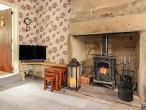 A cozy room with a stone fireplace, a television on a wooden shelf, and a small table with chairs. - Cobblers Cottage (Keighley)