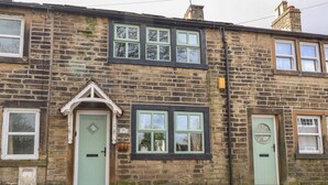 A two-story stone building with a traditional design, featuring a central entrance with a door and a small porch. - Cobblers Cottage (Keighley)