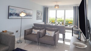 Ein modernes Wohnzimmer mit einem grauen Sofa, einer Stehlampe und einem Essbereich mit Tisch für zwei Personen.