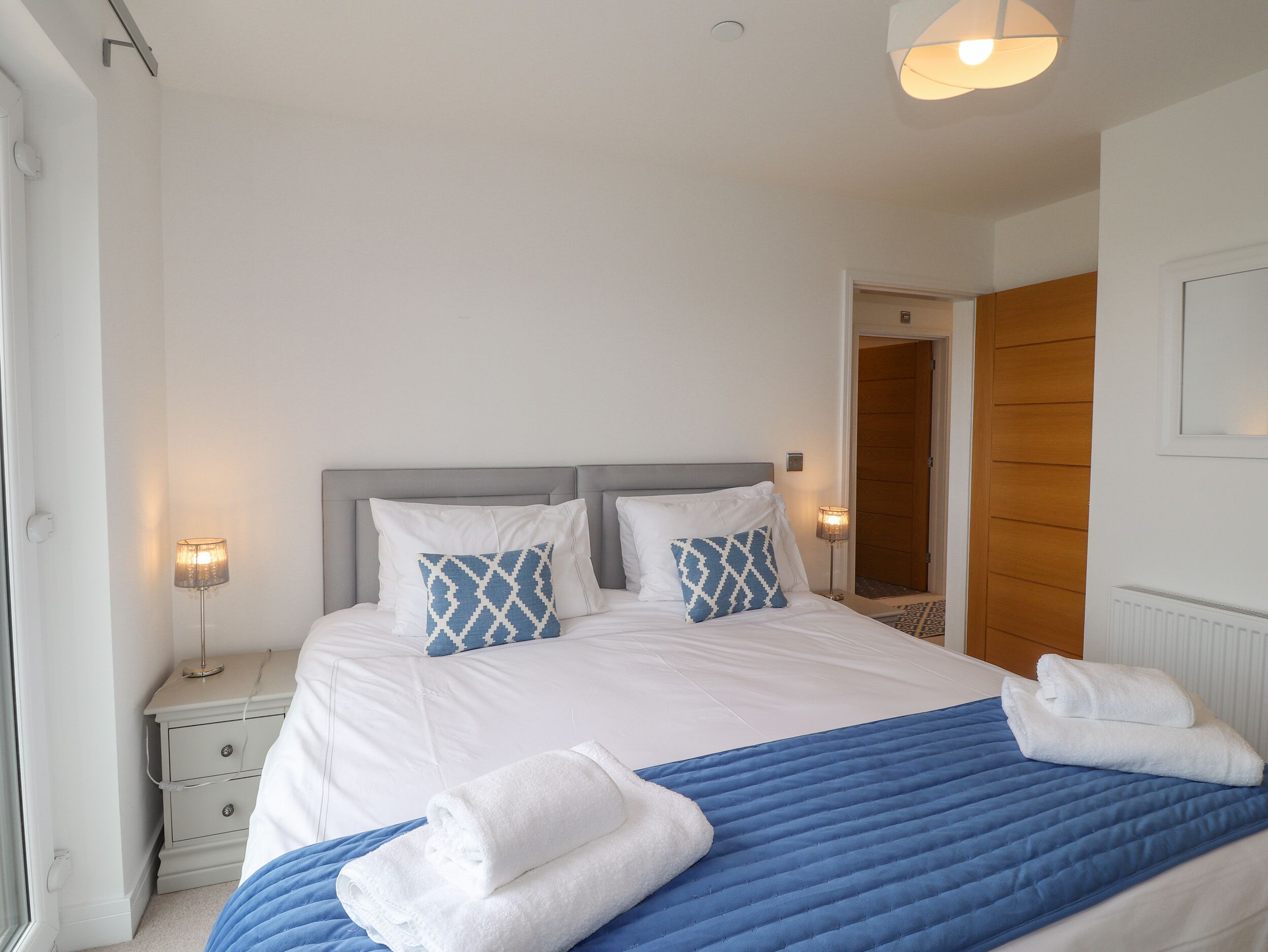 Un lit bien fait, avec des oreillers blancs et bleus à motifs, une couverture bleue et des serviettes blanches pliées sur le lit.