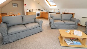 Ein gemütliches Wohnzimmer mit zwei grauen Sofas, einem Holztisch und einer Küche im Hintergrund.