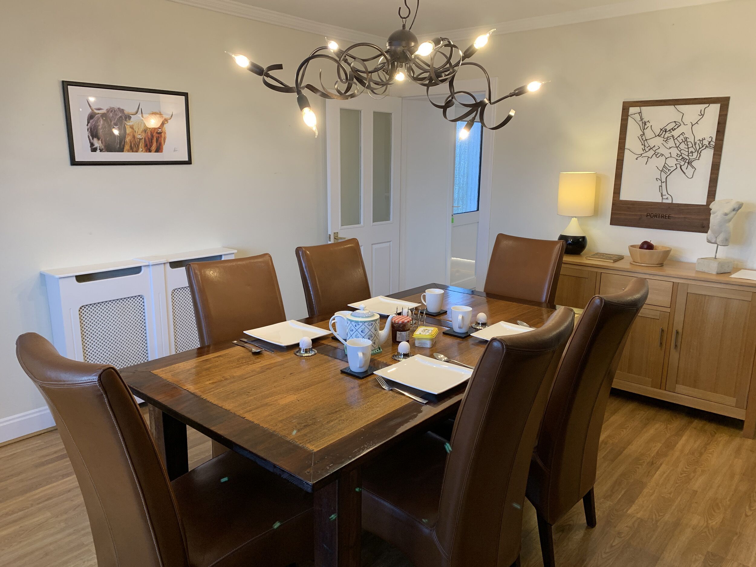 A dining area with a wooden table, brown leather chairs, a chandelier, and artwork on the walls.