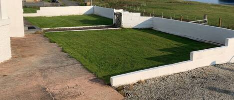 A residential property with a well-maintained lawn, a white fence, and a view of the sea and hills in the background.