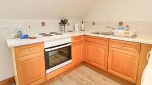 Una cocina con armarios de madera, horno empotrado, estufa y pileta.