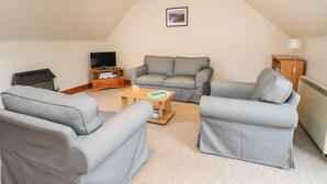 Una sala de estar acogedora con un sofá gris, una mesa de centro de madera y un televisor sobre un mueble.