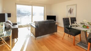 Un salon moderne avec un canapé, une table basse en verre et un coin repas avec une table dressée pour deux personnes.