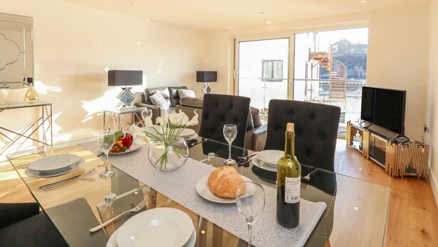 Un salon moderne avec un coin repas, comprenant une table en verre, des sièges confortables, un téléviseur et une vue sur l’extérieur.