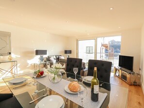 A modern living room with a glass dining table, comfortable seating, a television, and a view of the outside.