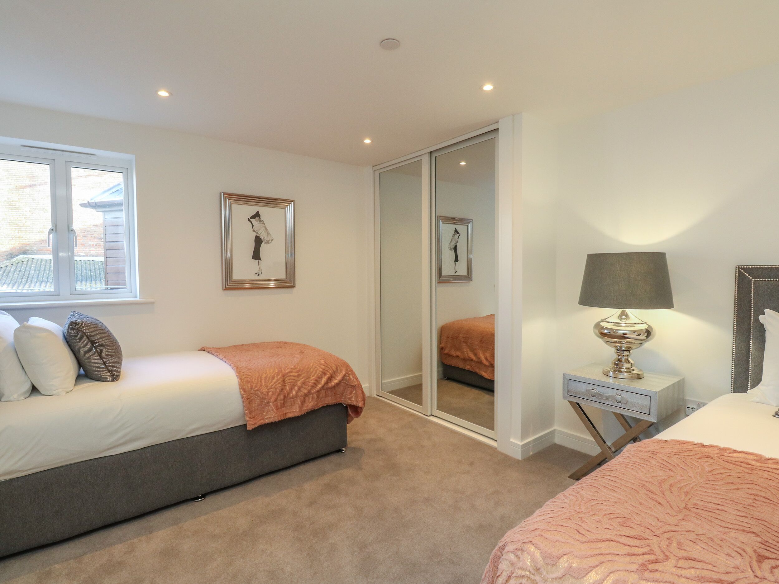 Ett sovrum med en säng, ett nattduksbord, en lampa, en spegel och ett fönster.