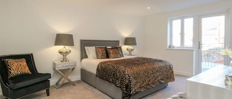 A bedroom with a bed, two bedside tables with lamps, a chair, a bench, and a window with a view.