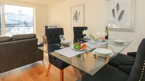 Un espace de repas moderne avec une table en verre, des chaises à revêtement noir et une vue sur la ville grâce à de grandes fenêtres.