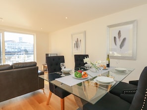 A modern dining area with a glass table, black upholstered chairs, and a view of the city through large windows.