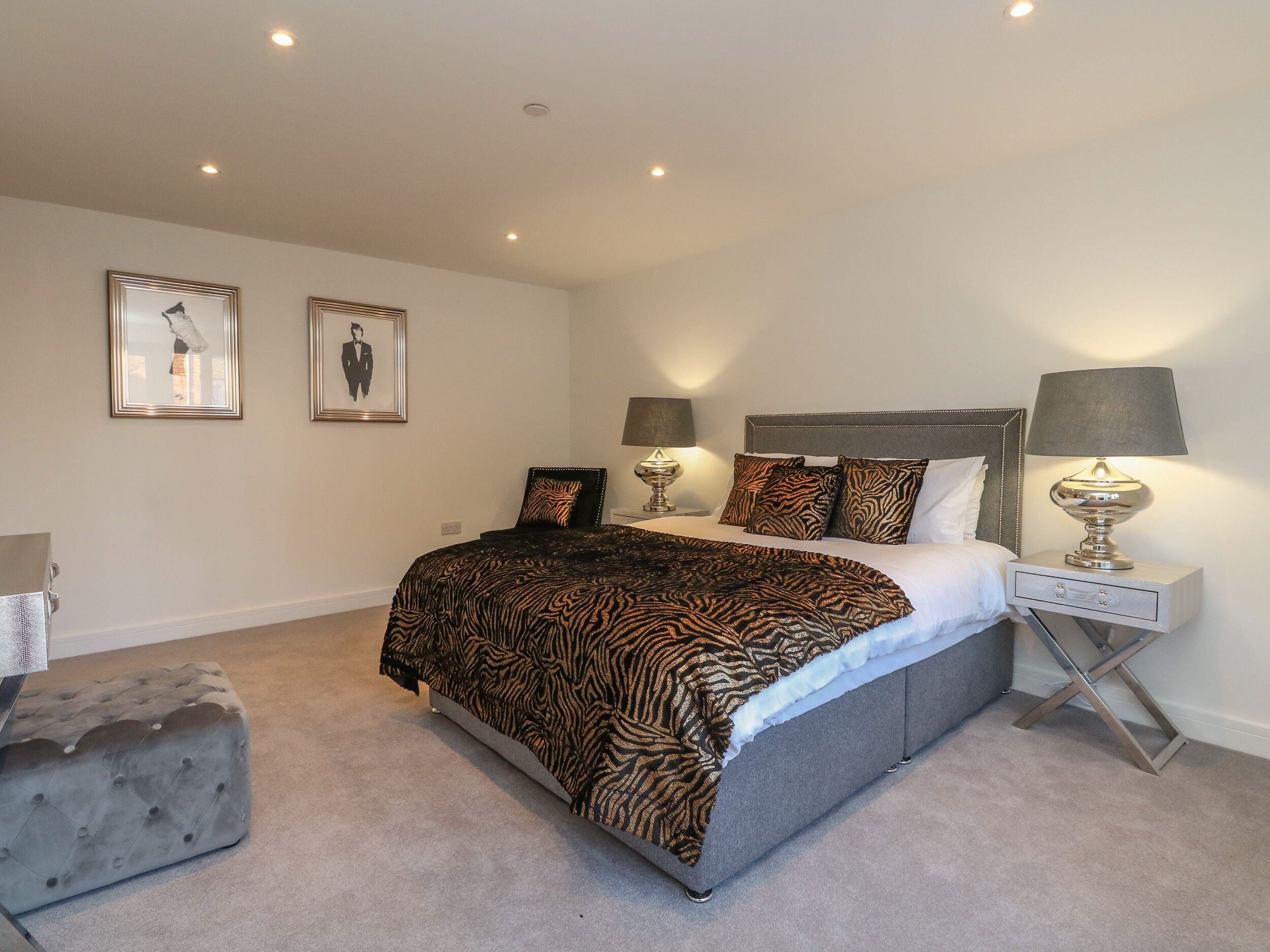 A bedroom with a large bed, two bedside lamps, a nightstand, and two framed pictures on the wall.