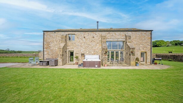A stone building with a patio area, outdoor seating, and a hot tub.